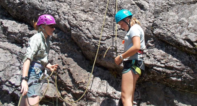 an outward bound student checks their knots while an instructor looks on 